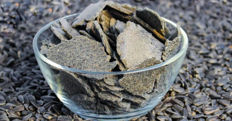 A glass bowl filled with sule seed cake on a bed of sunflower seeds.