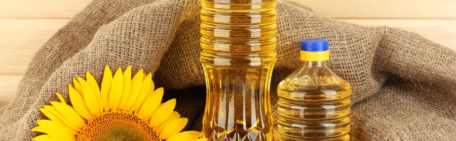 Two bottles of Sule sunflower oil next to a sunflower on a textured background.